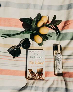 Wander + Ivy wine bottle laying on blanket with a book and lemons.